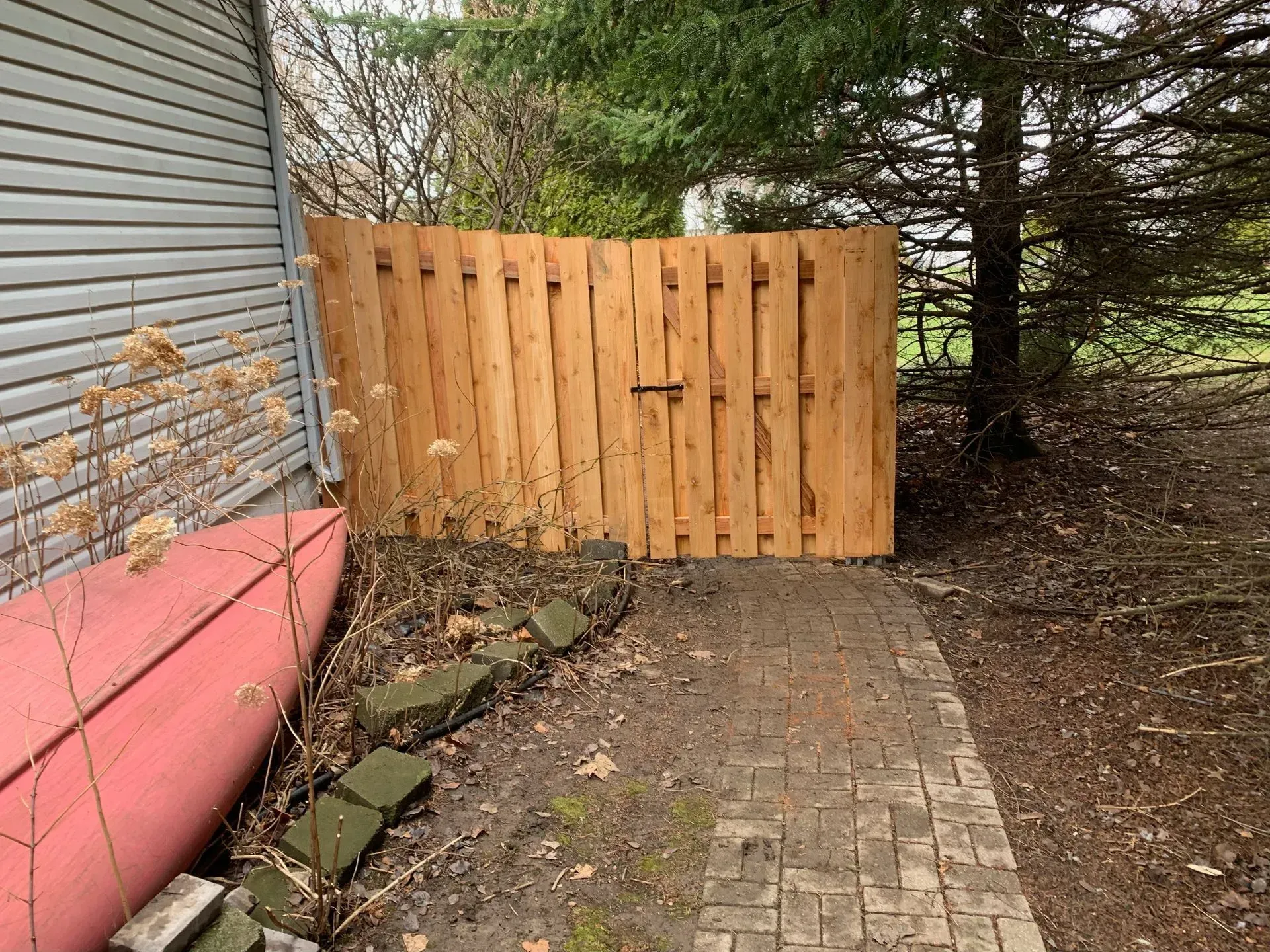 A wooden fence is sitting next to a brick walkway.