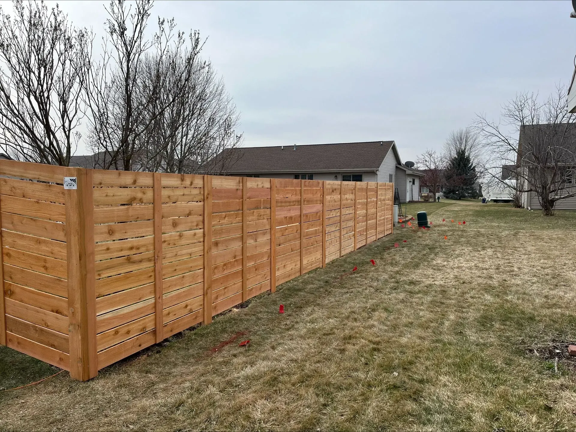 A wooden fence is sitting in the middle of a grassy field next to a house.