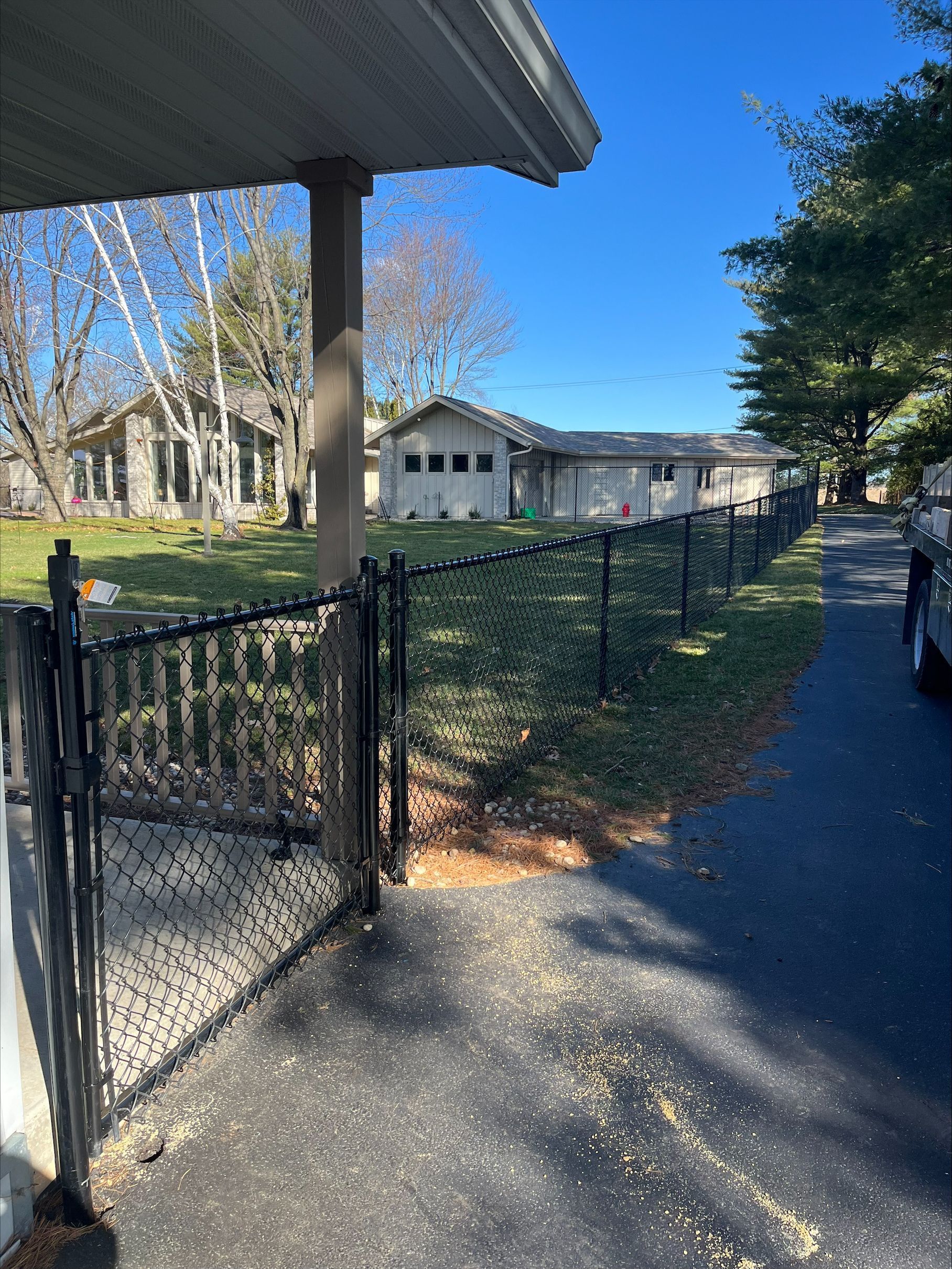 A chain link fence surrounds a driveway in front of a house.