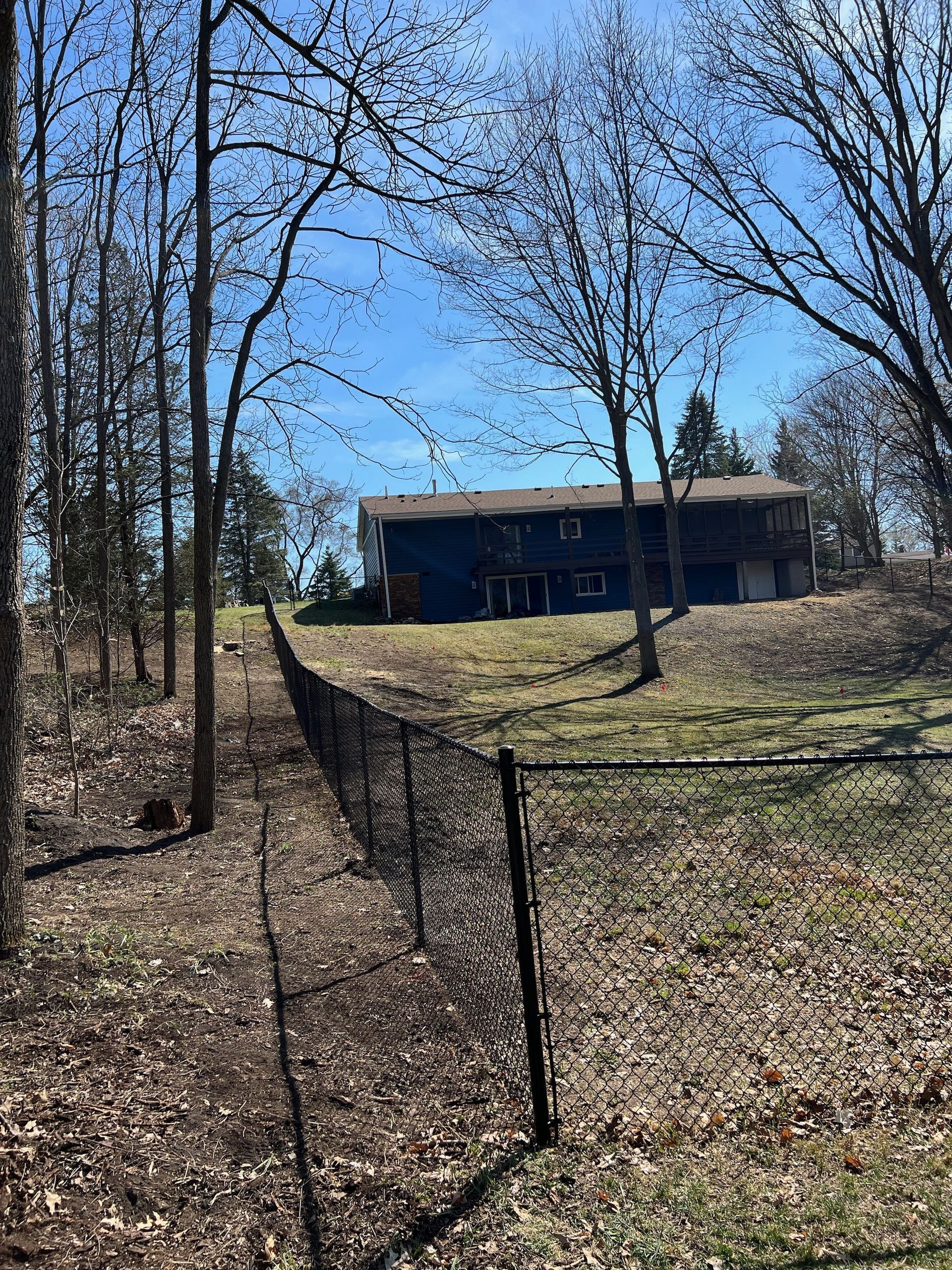 A blue house is surrounded by trees and a black fence.