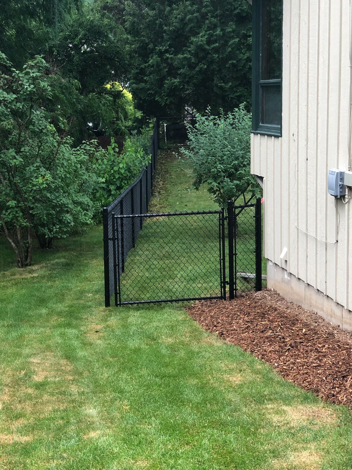 A chain link fence with a gate in the backyard of a house.