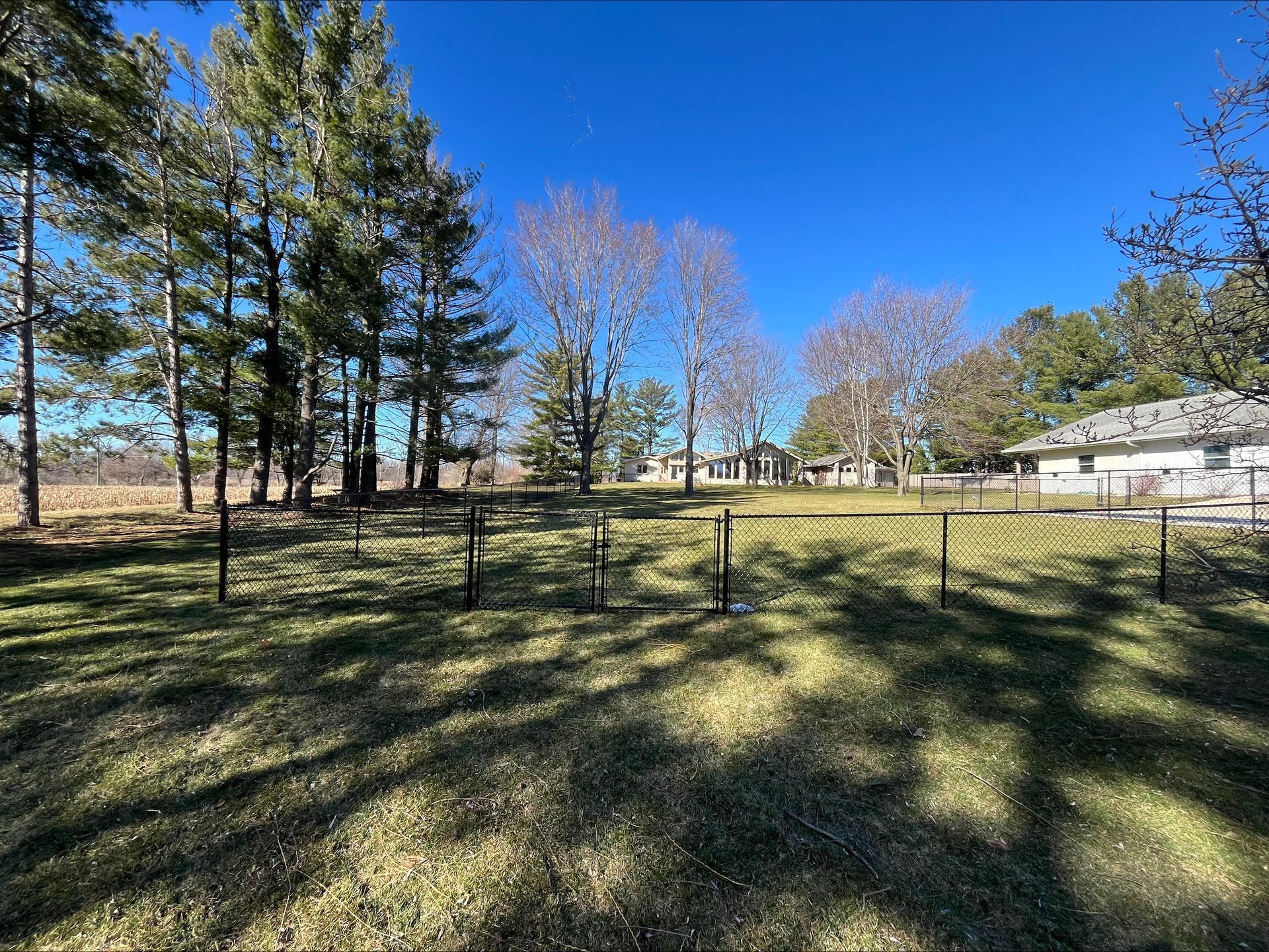 A large grassy field with trees in the background and a house in the background.