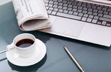Laptop with newspaper, coffee, and pen