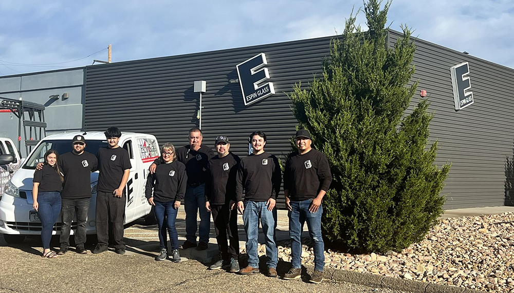 A man stands beside a white work van with company logos under a blue sky.
