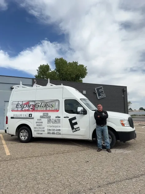 A man stands beside a white work van with company logos under a blue sky.