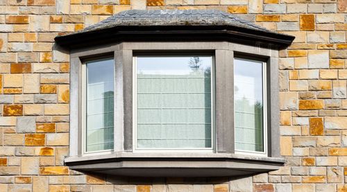 Bay window with three panes, set in a brick wall. Includes a dark stone trim and roof-like ledge.