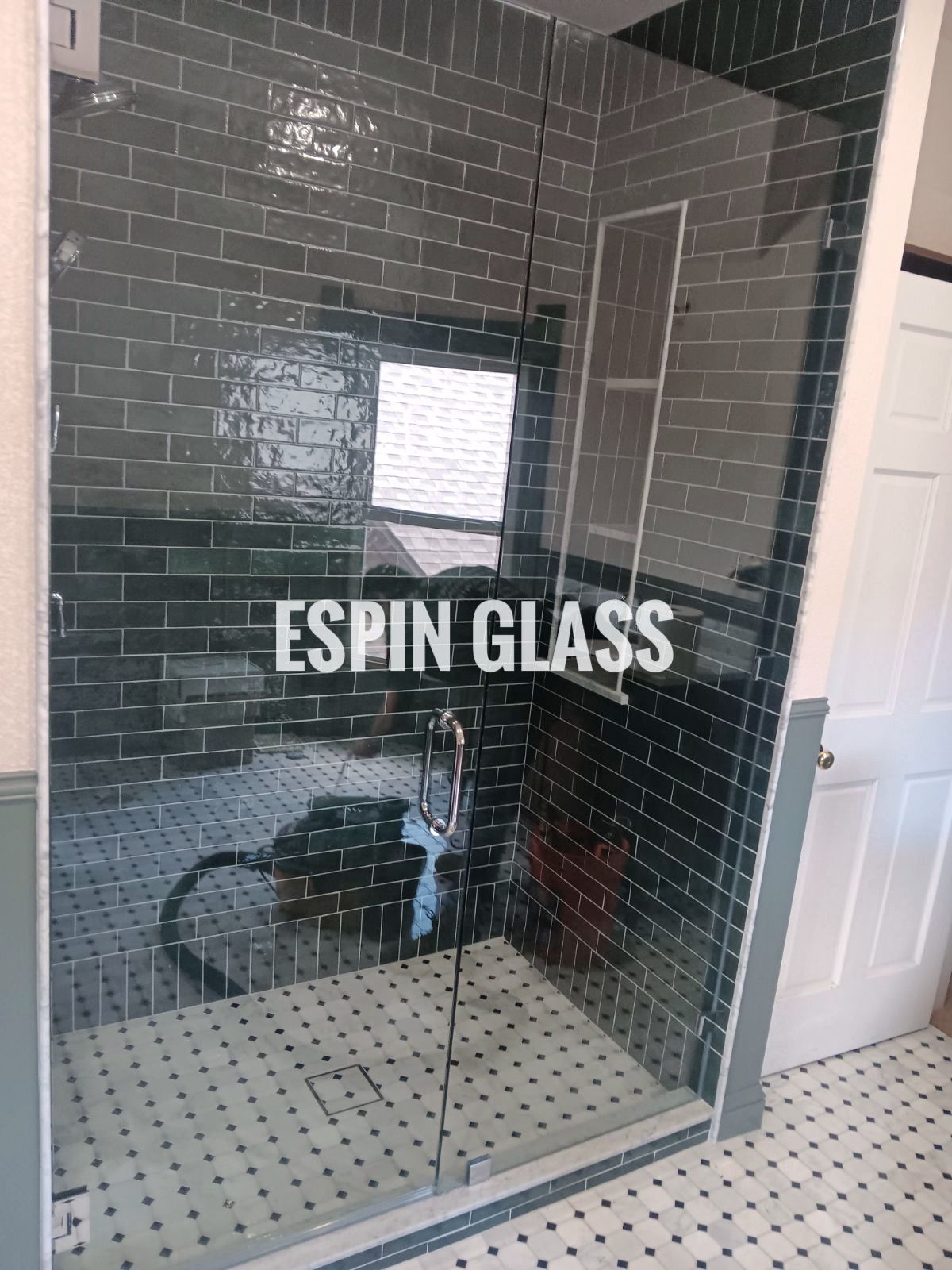 Glass shower enclosure with green tile, black and white floor.