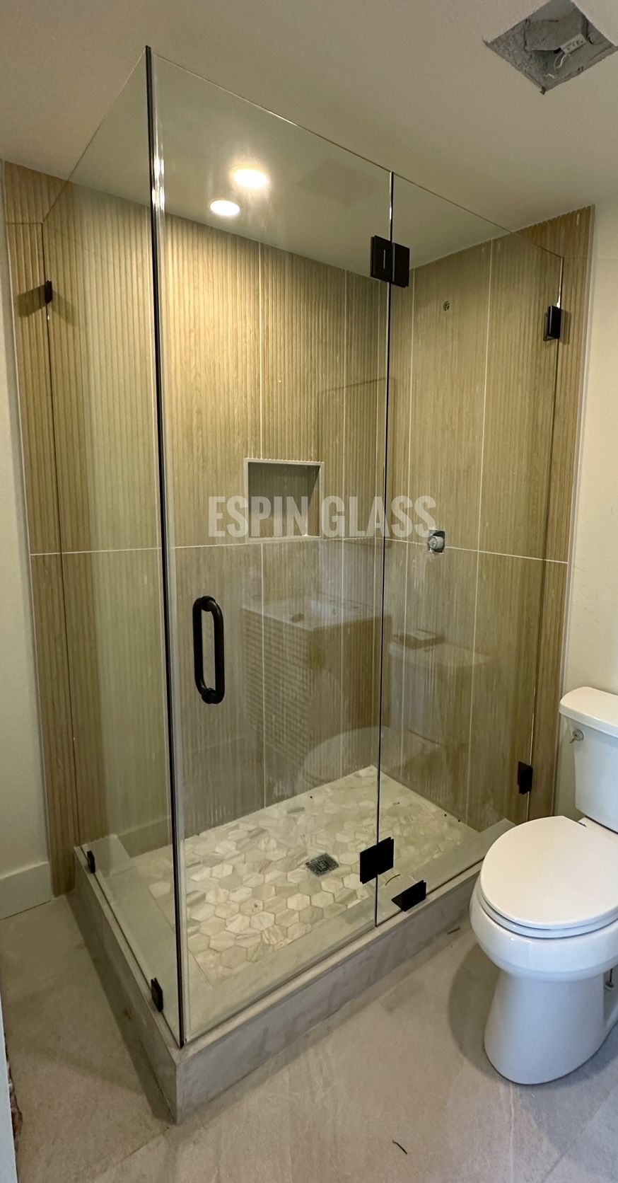 Frameless glass shower with black hardware in a neutral-toned bathroom.