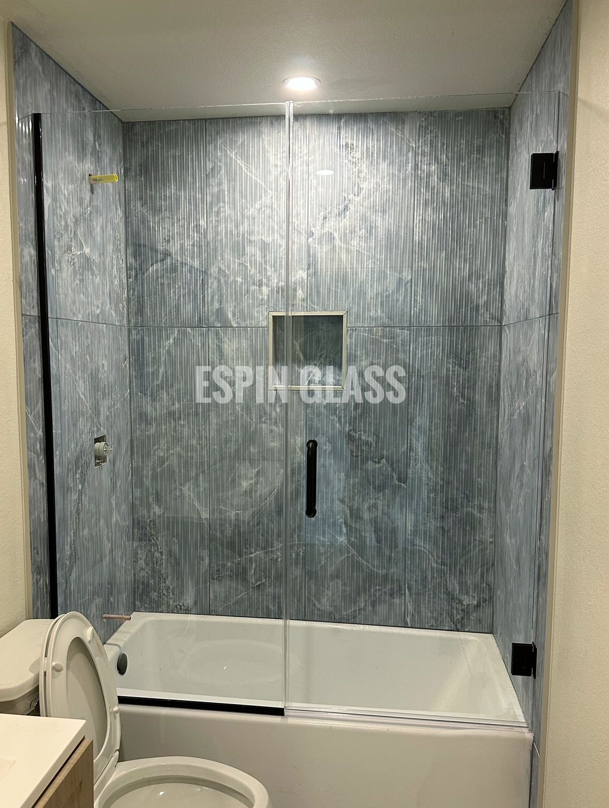 Bathroom with textured blue walls, tub, glass door, and black hardware.