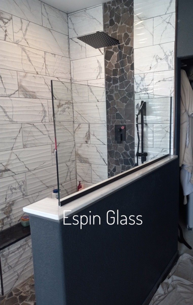 Modern shower with glass partition, marble tile, dark gray wall, black shower head.
