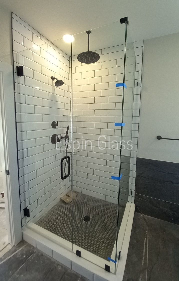 Glass shower with black fixtures, white brick wall, and black tiled floor.