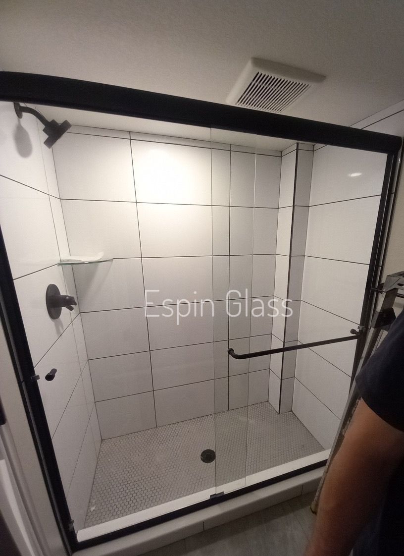 Black-framed glass shower enclosure with black fixtures on white tiled walls; interior.
