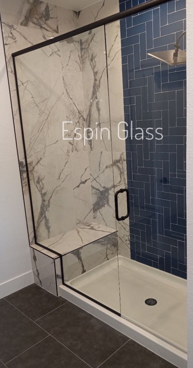 Shower with marble-look wall, glass door with black frame, blue tiled wall, and built-in seat.
