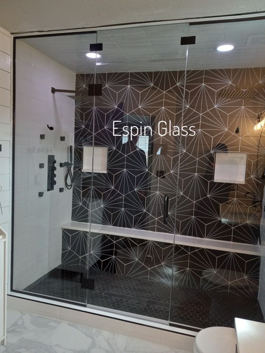 Glass shower enclosure with black tile, a bench, and chrome fixtures.