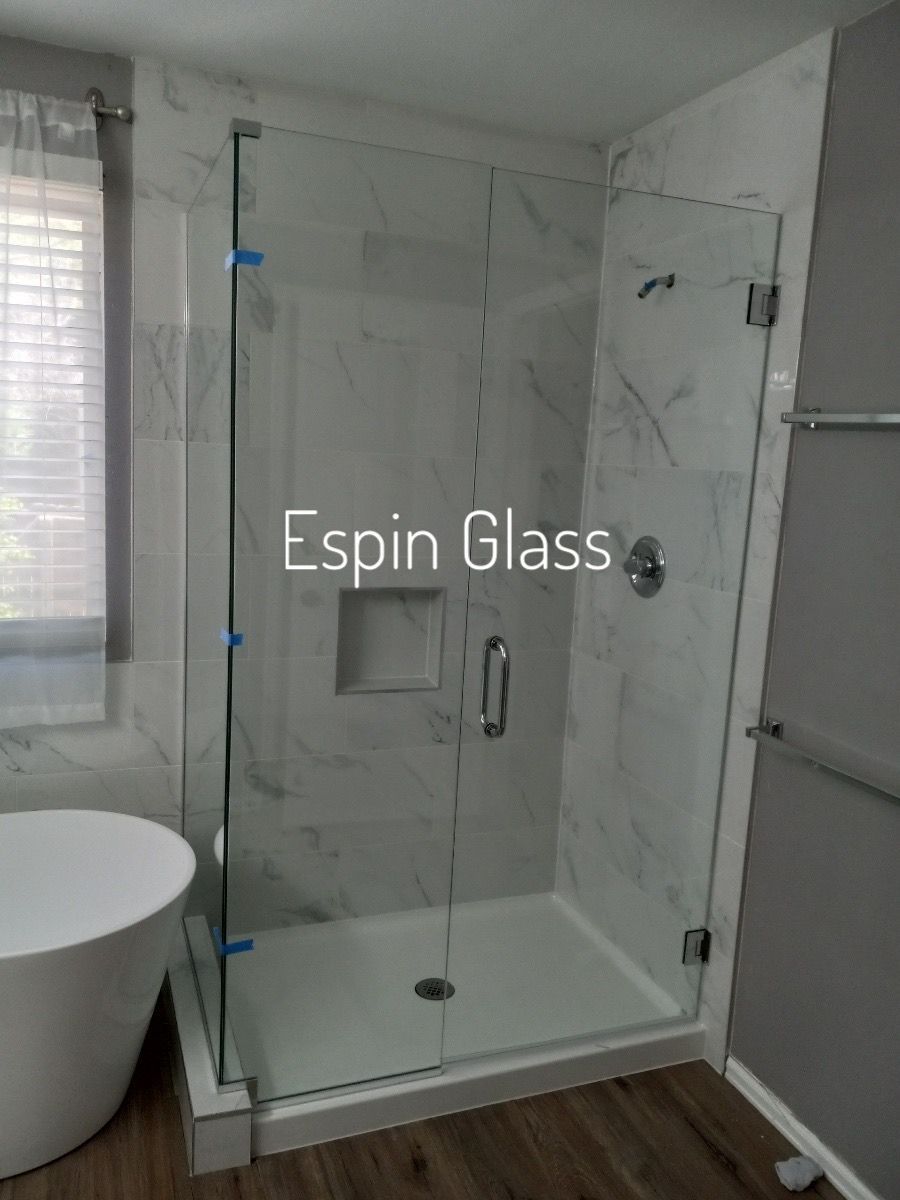 Glass shower enclosure with marble-look tile, and a white bathtub in a bathroom.