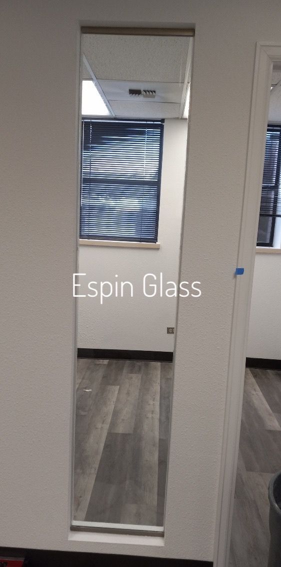 A narrow mirror inset in a white wall reflects an office interior with a window, flooring, and the 