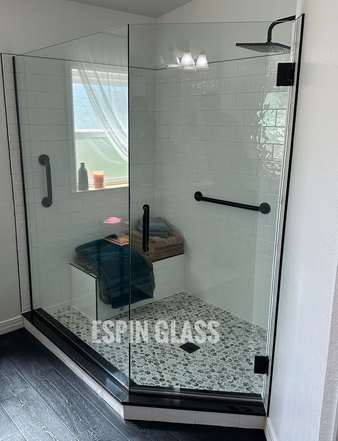 Corner shower with black trim, mosaic floor, bench, and grab bars.