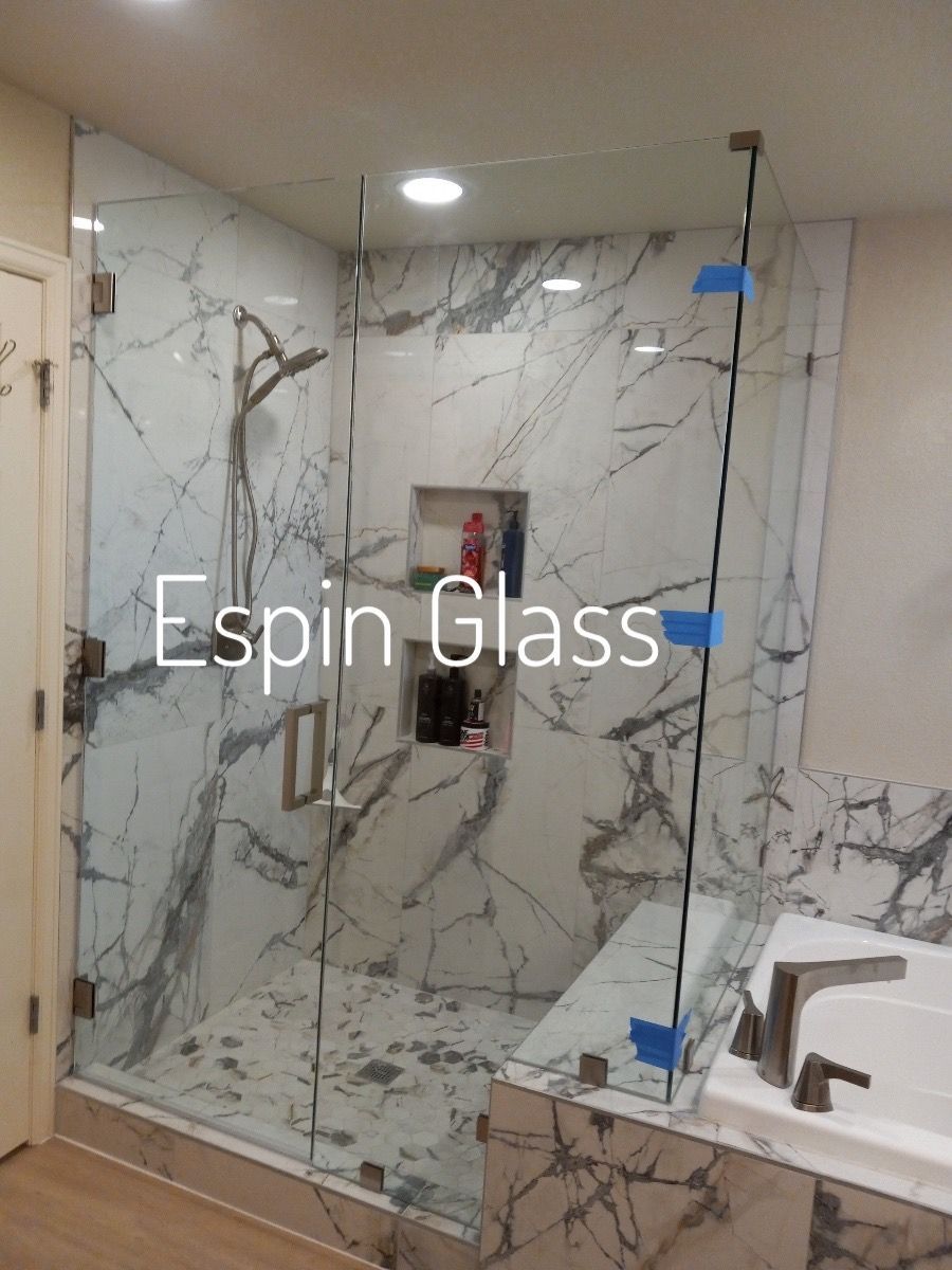 Glass shower enclosure with marble-look tiles, brass hardware.