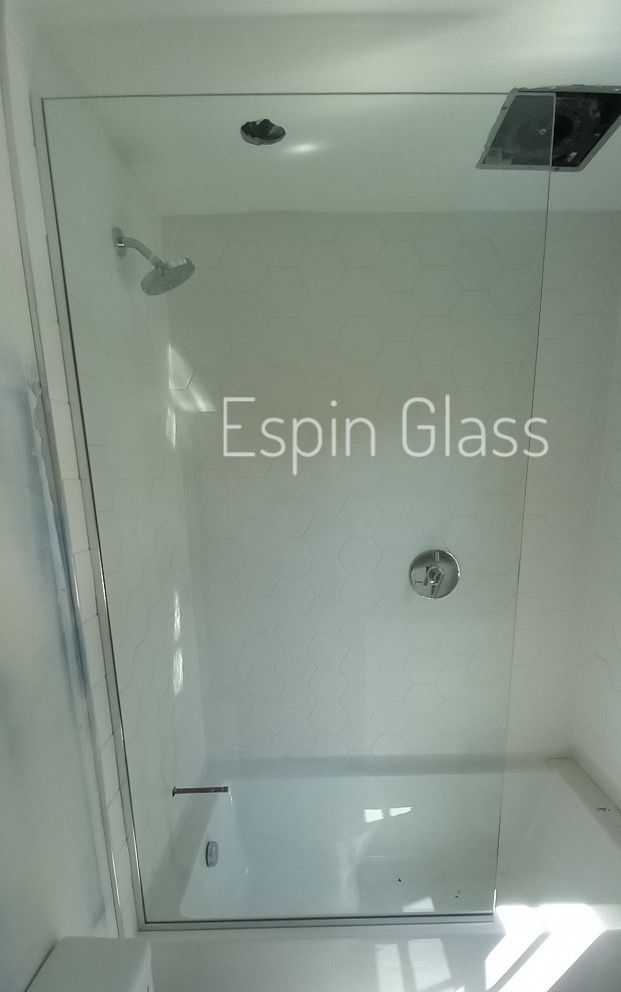 Clear glass shower enclosure with showerhead and fixtures; white walls.