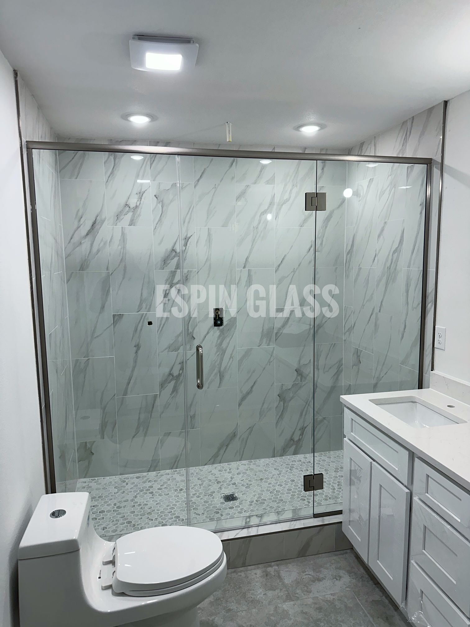 Bathroom with glass shower door, white vanity, toilet, and marble-look tile.