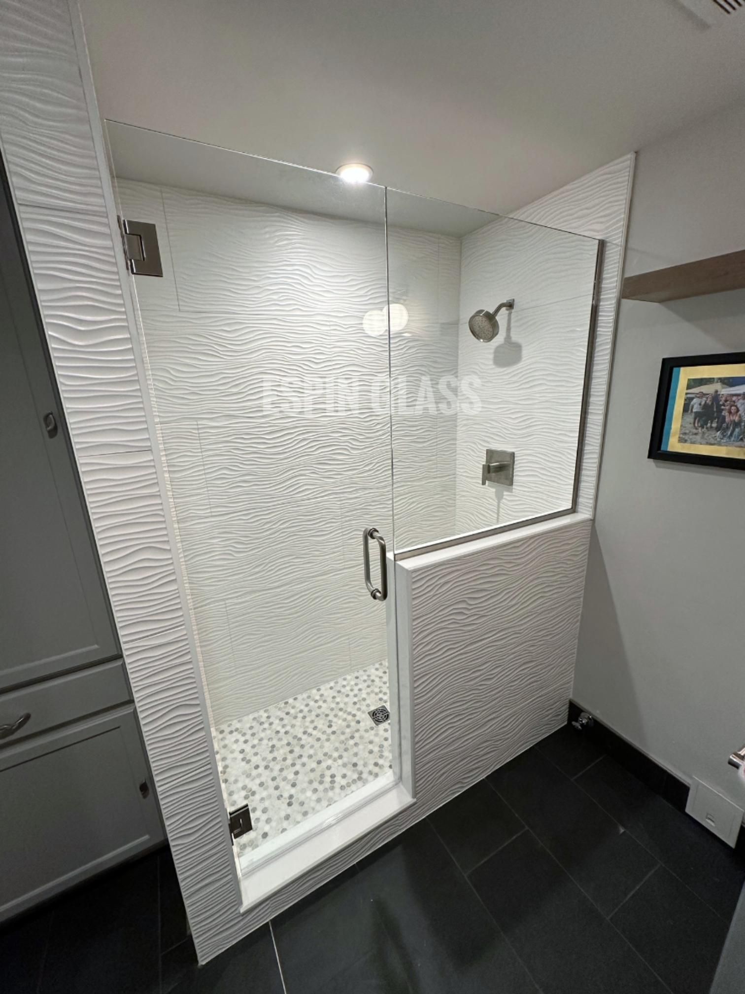 Modern white-tiled shower with glass door and black tile floor. Silver shower head and fixtures.