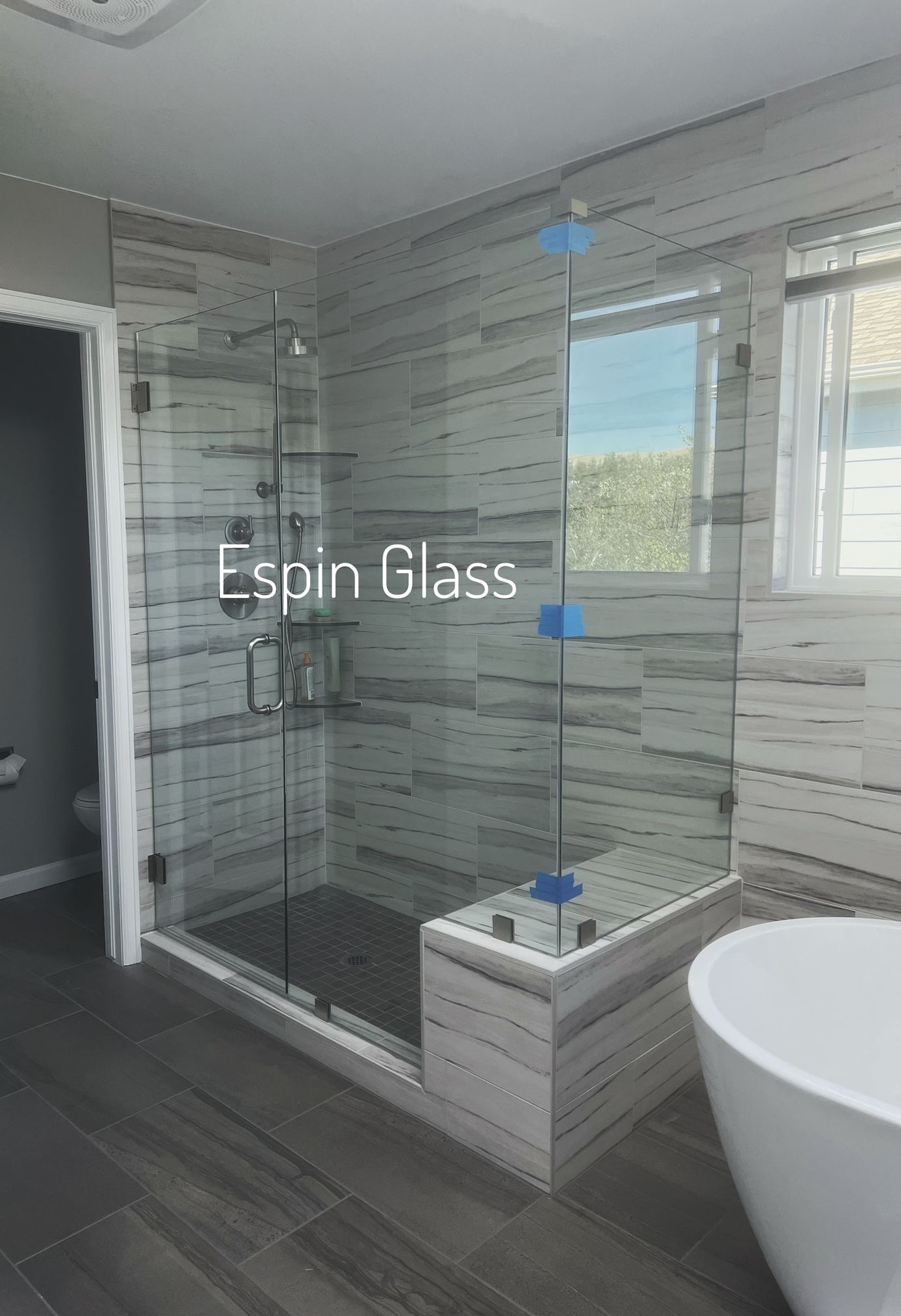 Glass shower enclosure in modern bathroom with bench and soaking tub.