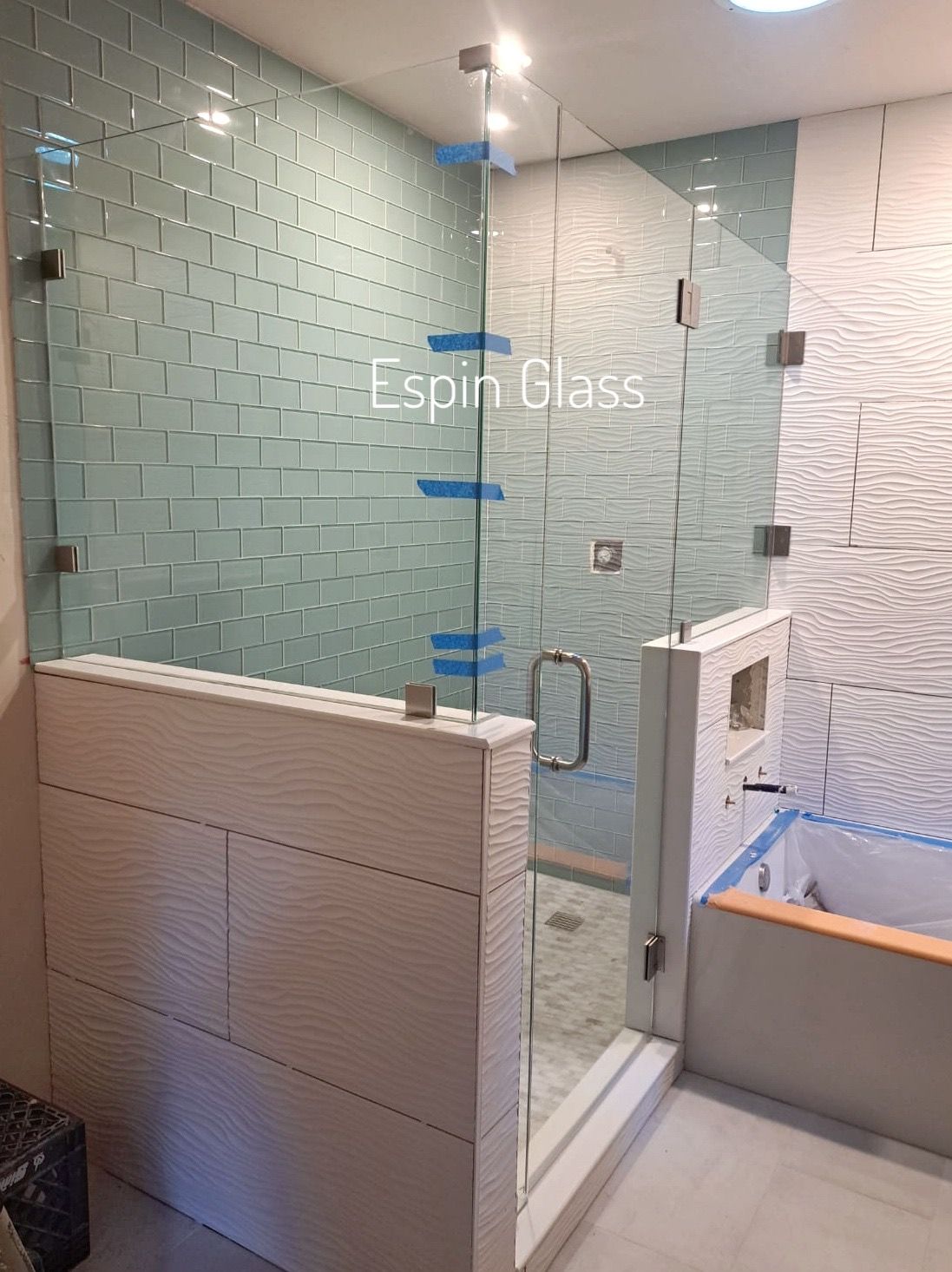 A modern bathroom with a glass shower. Teal and white tile walls and a white vanity.