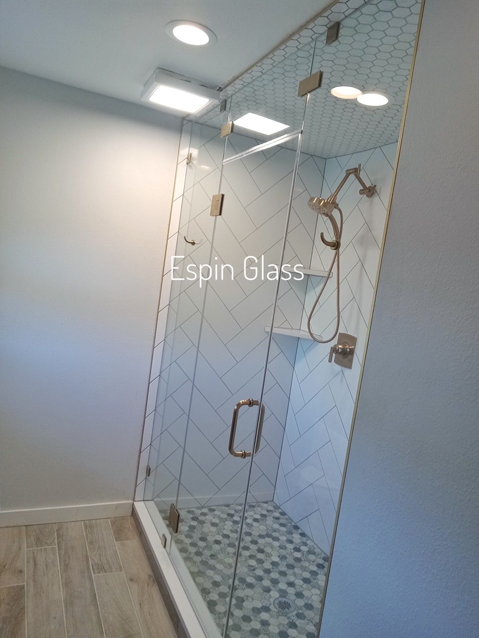 Glass shower enclosure with gold hardware, white and blue tile, neutral walls.