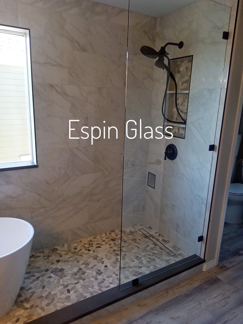 Modern bathroom with glass shower, marble tiles, and stone floor; showerhead and fixture.