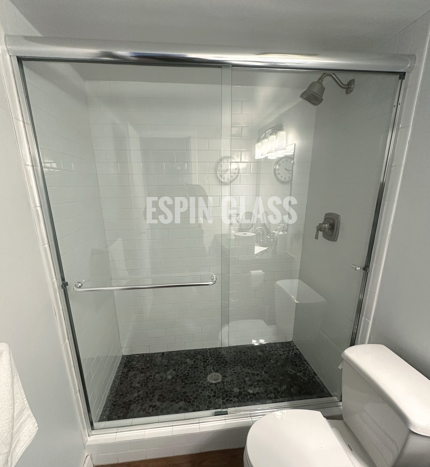 A glass shower enclosure with a gray stone floor, next to a white toilet.