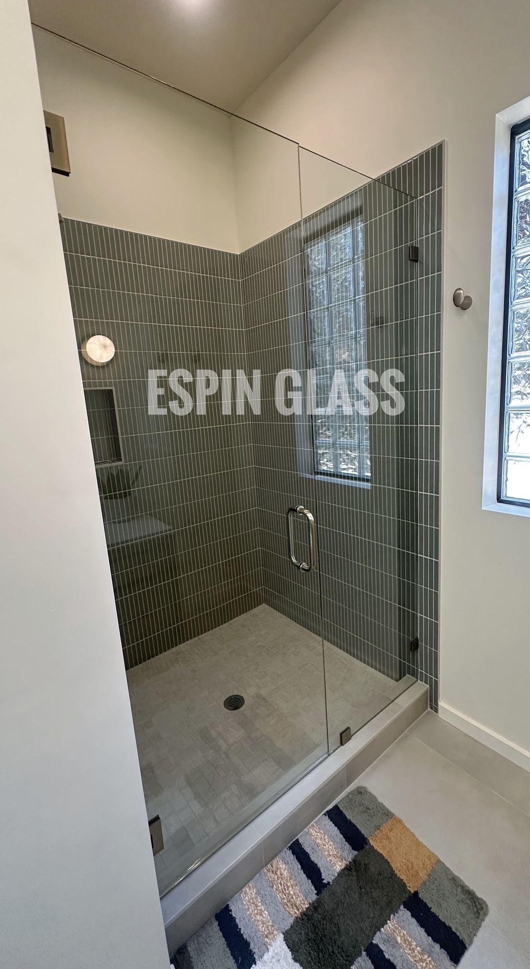 Modern shower with glass enclosure, gray wavy tile, and geometric rug.