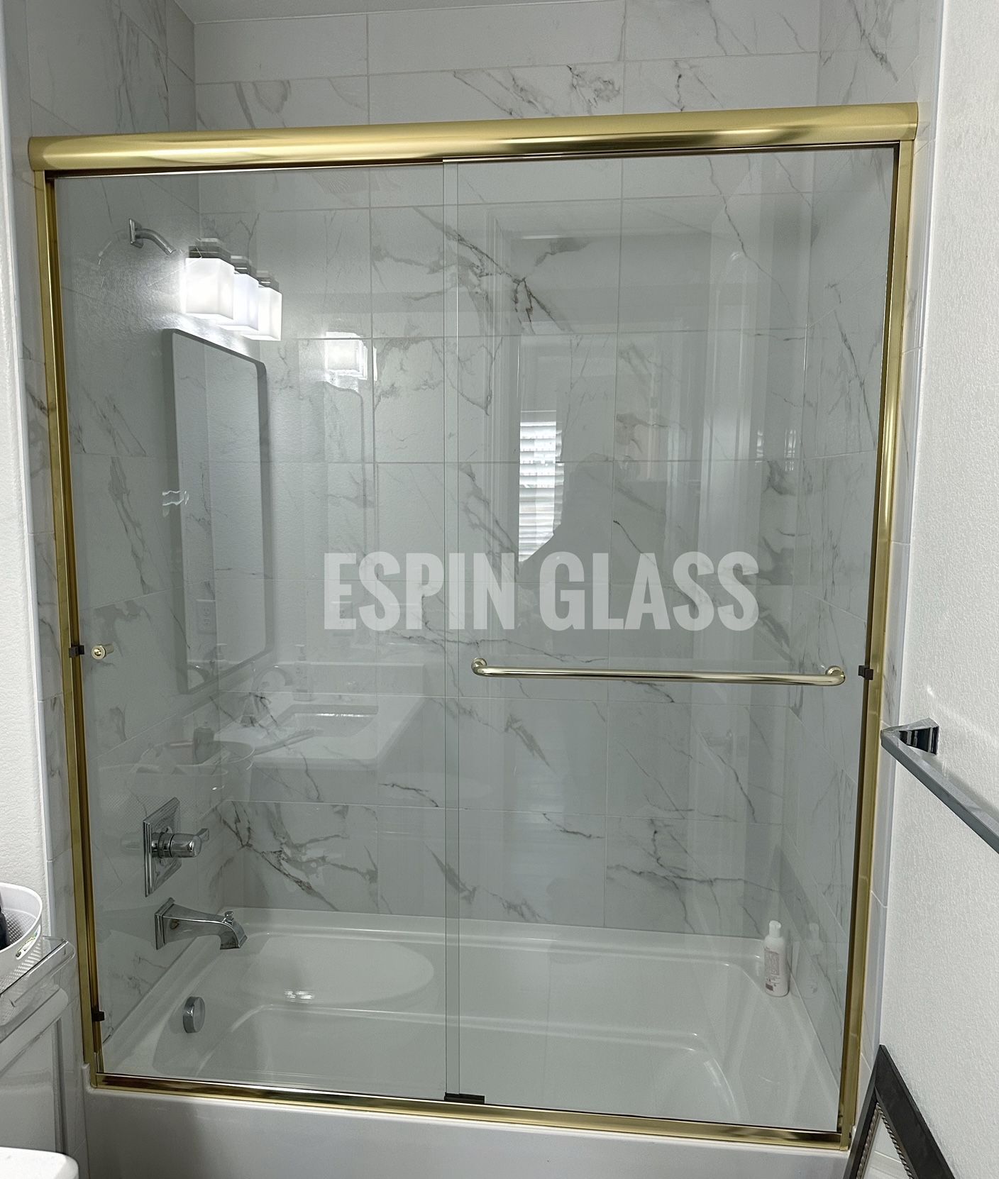 Gold-framed glass shower door in a marble-tiled bathroom.