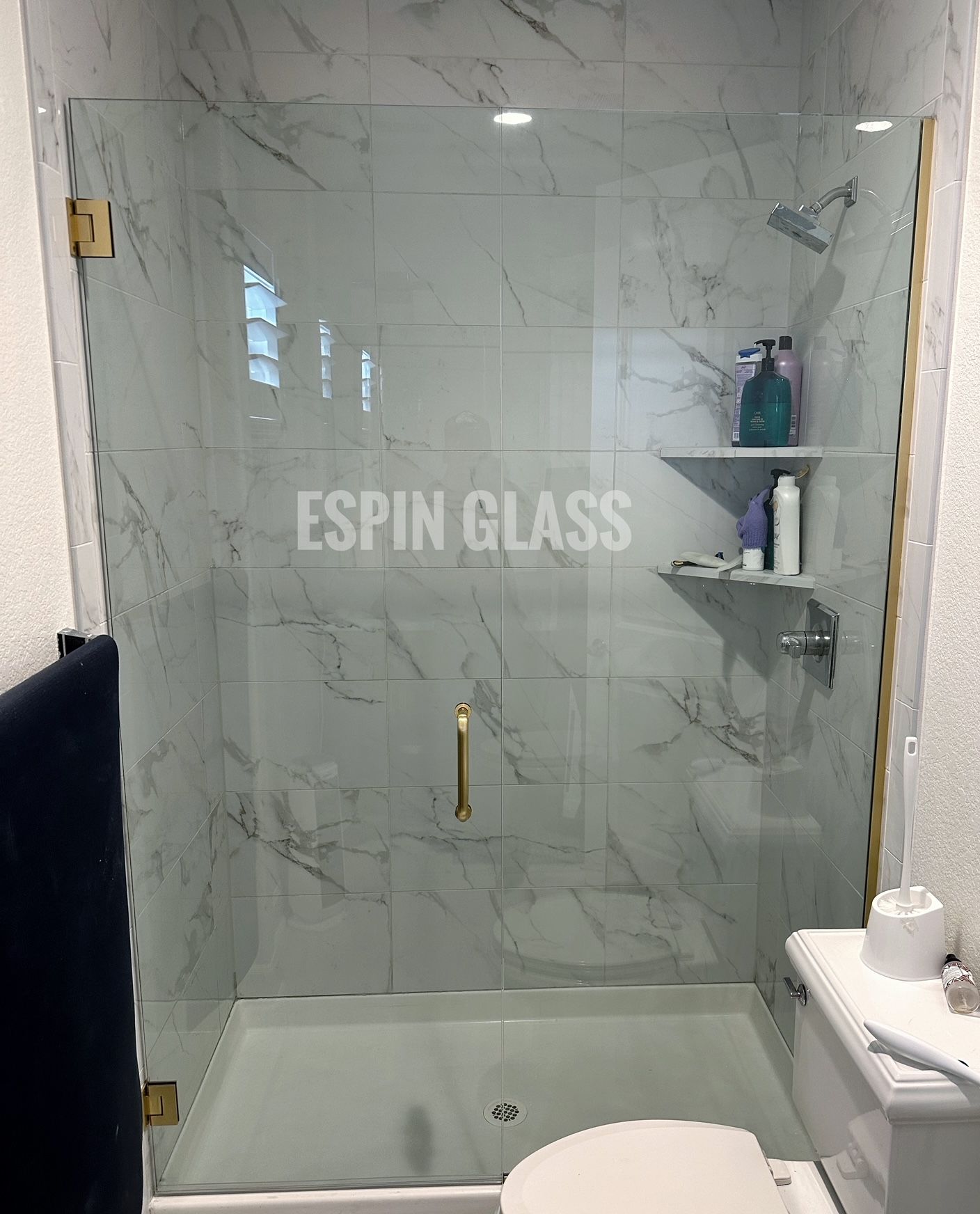 Glass shower enclosure with marble-patterned walls and gold hardware in a bathroom setting.