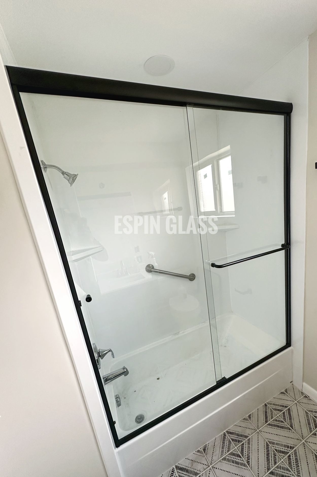 Black-framed sliding glass shower door over a white bathtub, with a grab bar.