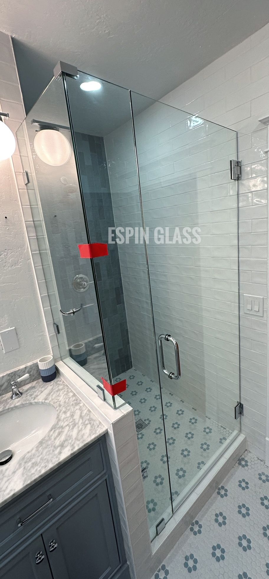Bathroom with frameless glass shower enclosure, white and gray tile, and gray vanity.