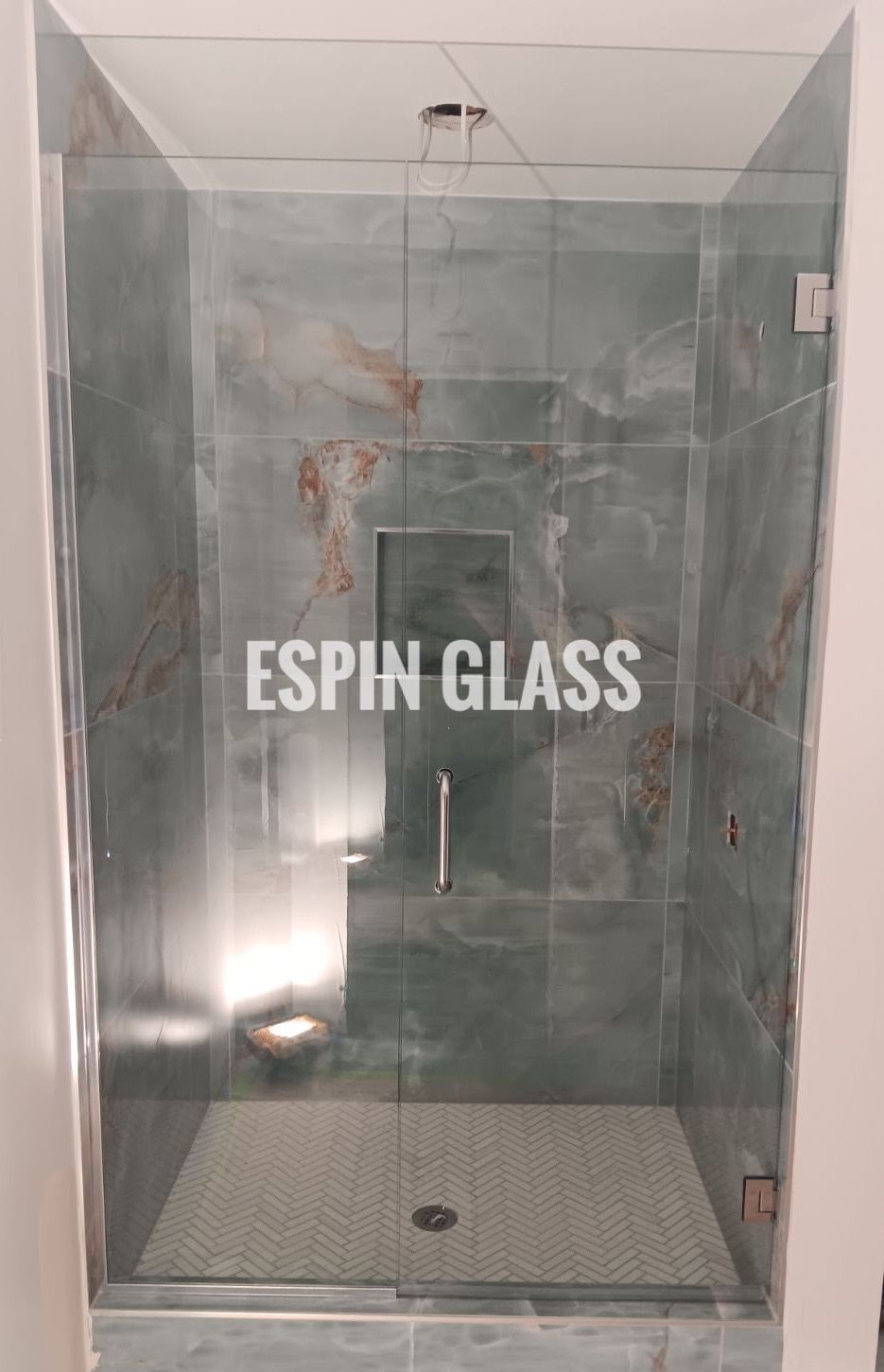 Glass shower enclosure with green marble walls and floor. Silver hardware and a glass door.