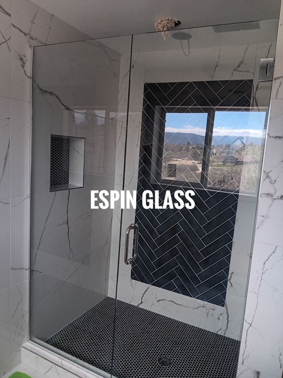 Glass shower enclosure with marble-look walls and a dark, patterned accent wall near a window.