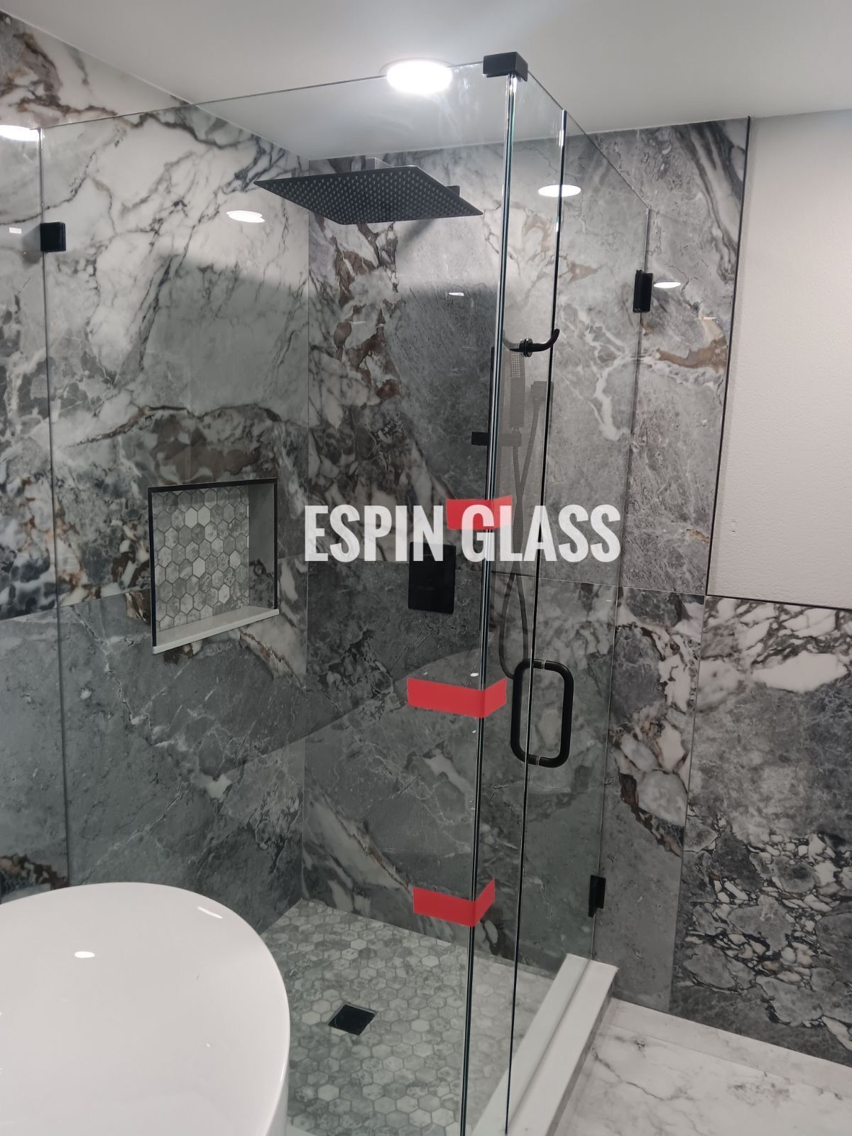 Glass shower enclosure with marble walls, black hardware.