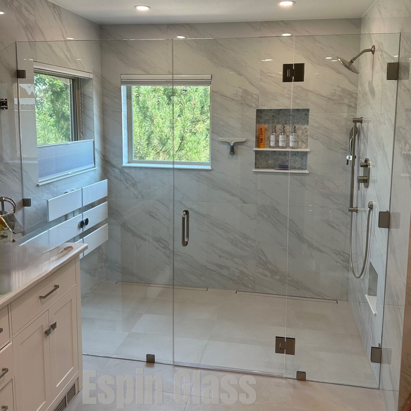Spacious bathroom with a frameless glass shower, white marble walls, and a vanity.