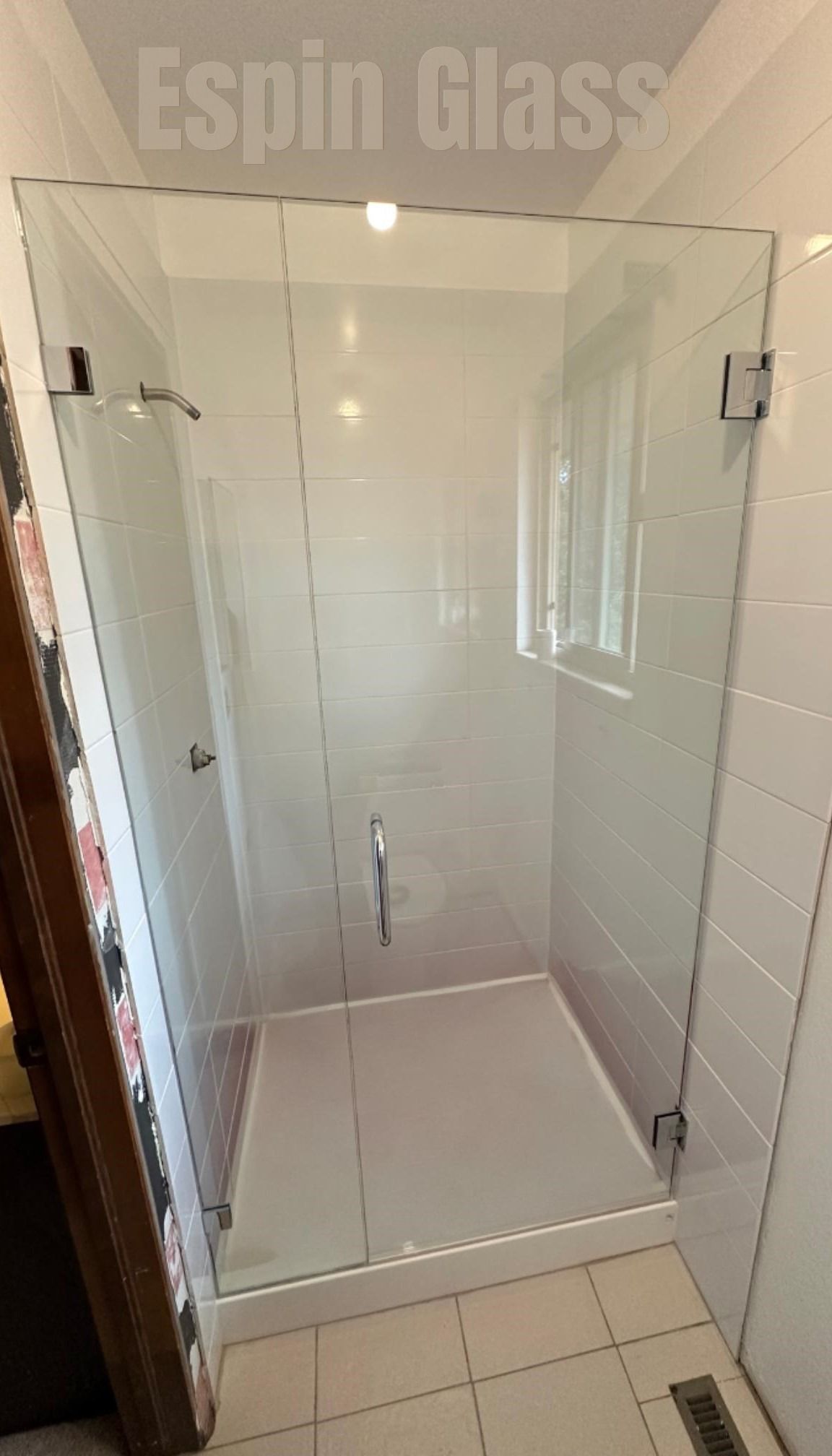 Glass shower enclosure in a white-tiled bathroom. Features a door and stationary panel, chrome hardware.
