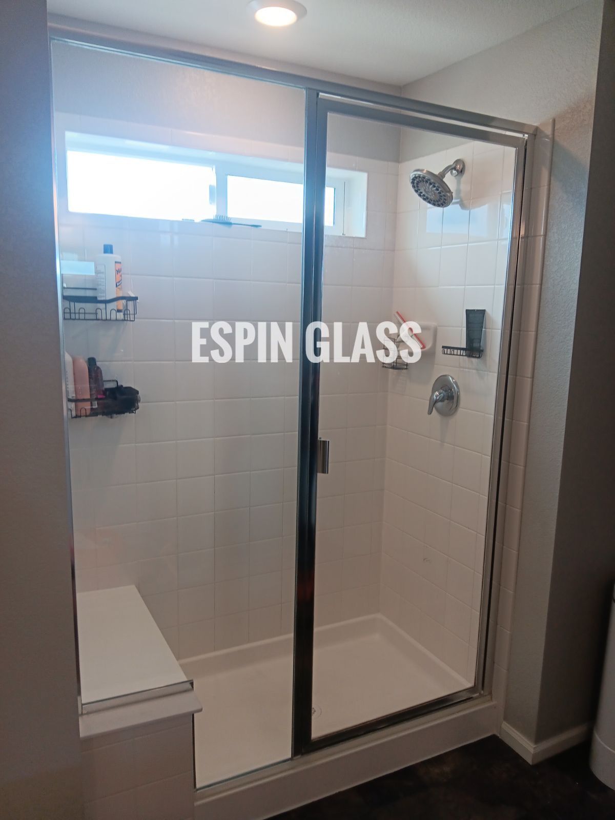Framed glass shower enclosure in a bathroom, white tile walls, chrome fixtures.