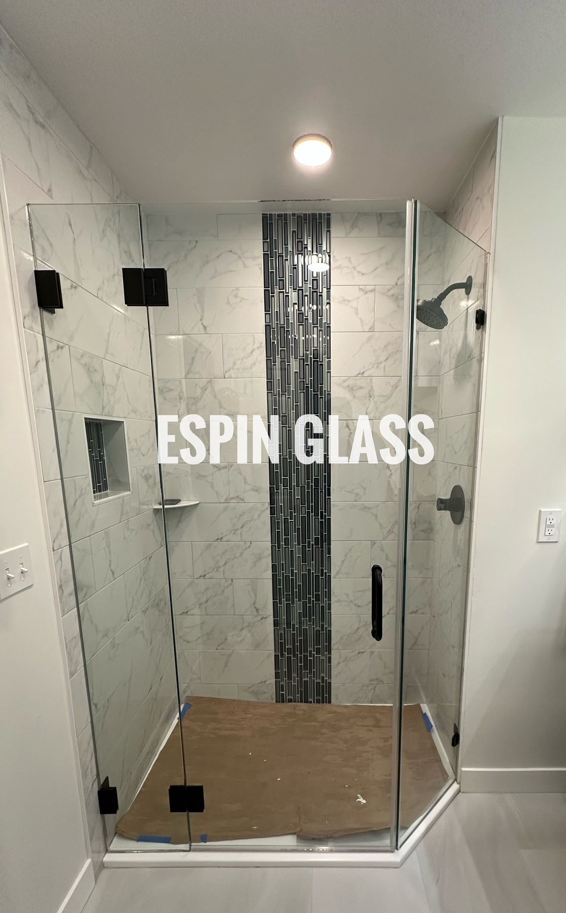 Frameless glass shower with black hardware, mosaic tile accent, and white marble-look tile walls.