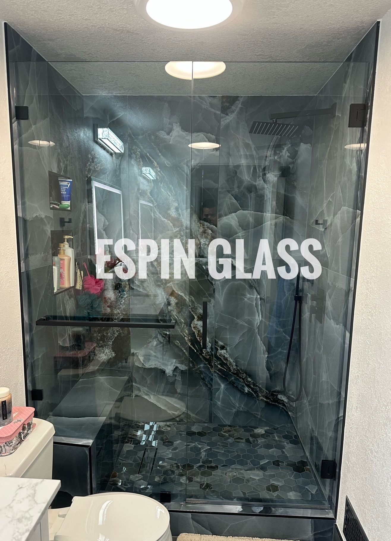 Modern shower with black frame, glass doors, and marble-like gray walls and floor; white toilet in foreground.