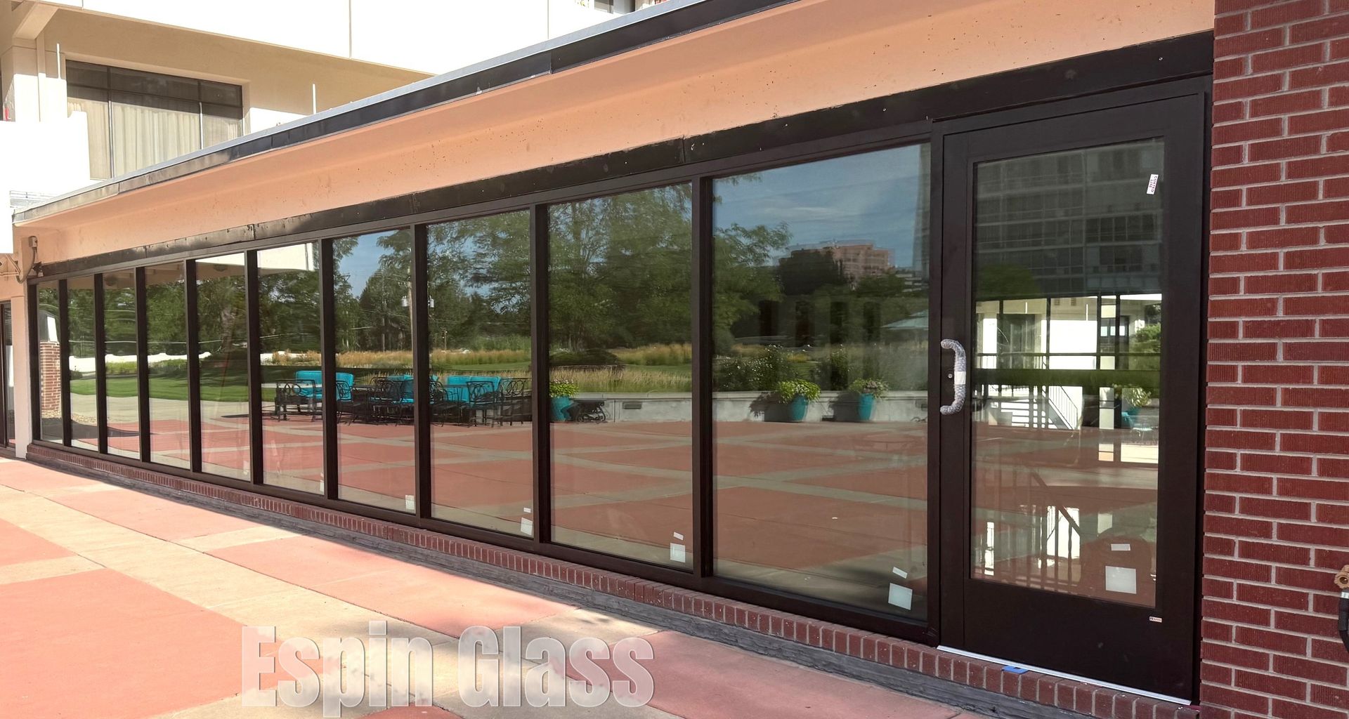 Building with large windows reflecting the outdoors. Red brick and tan accents.