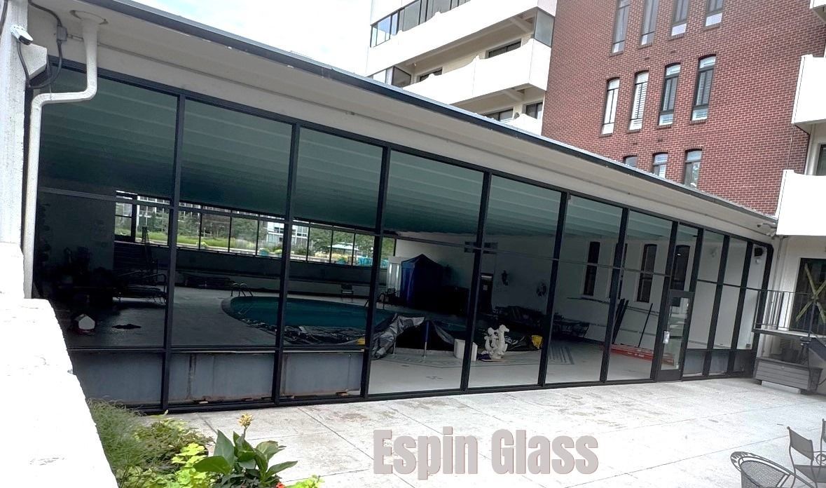 A glass-walled pool enclosure with a pool, with a building in the background.