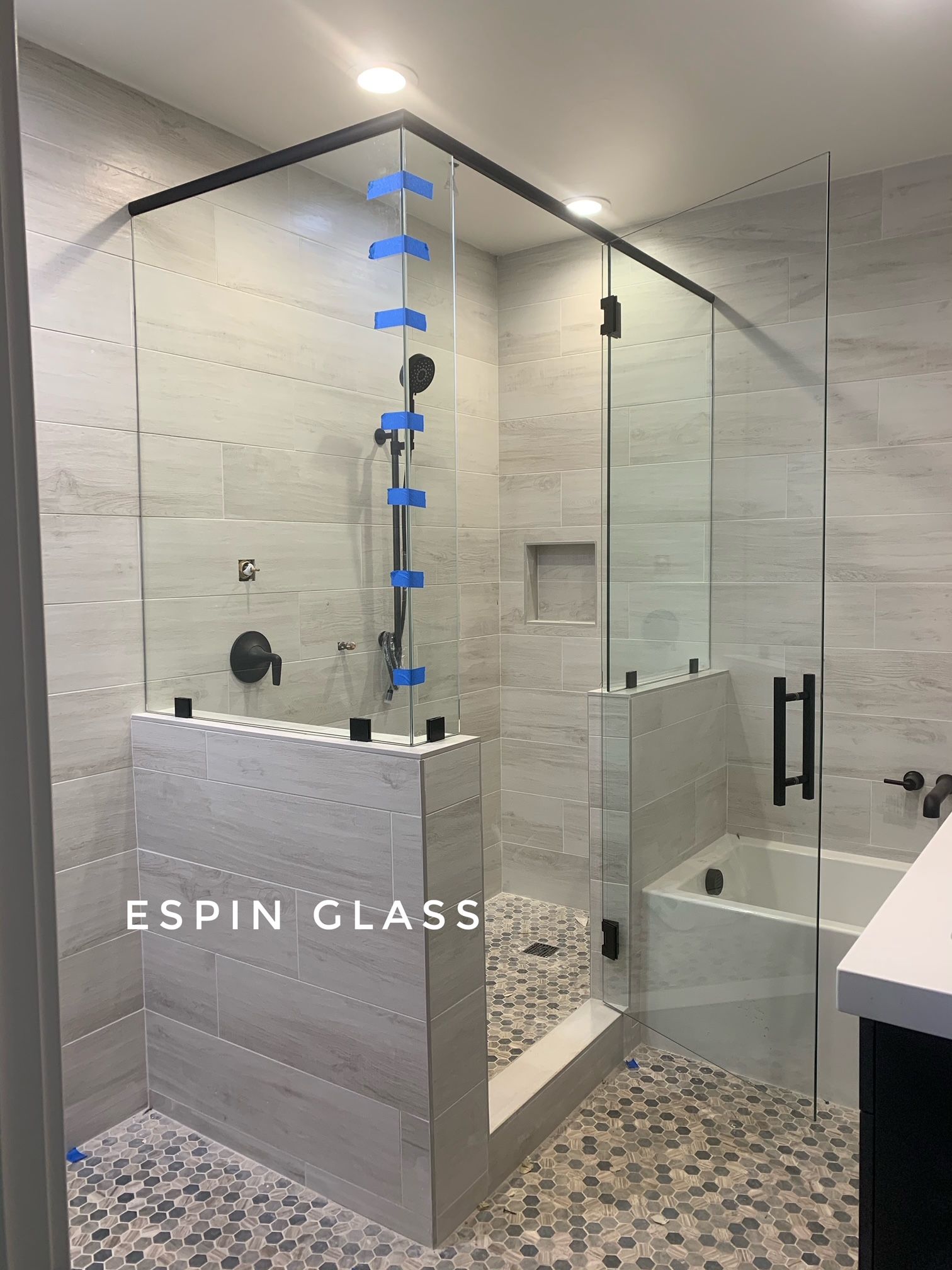 Corner glass shower enclosure with black hardware in a modern bathroom.