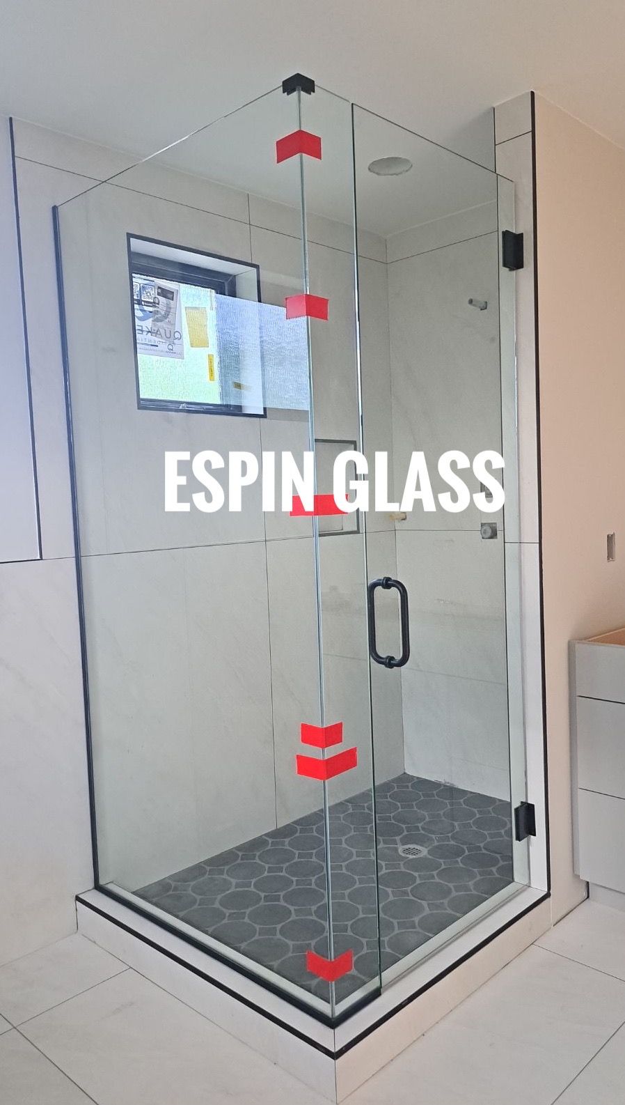 Glass shower enclosure in a bathroom. Features clear glass, black hardware, and a black and white tiled floor.