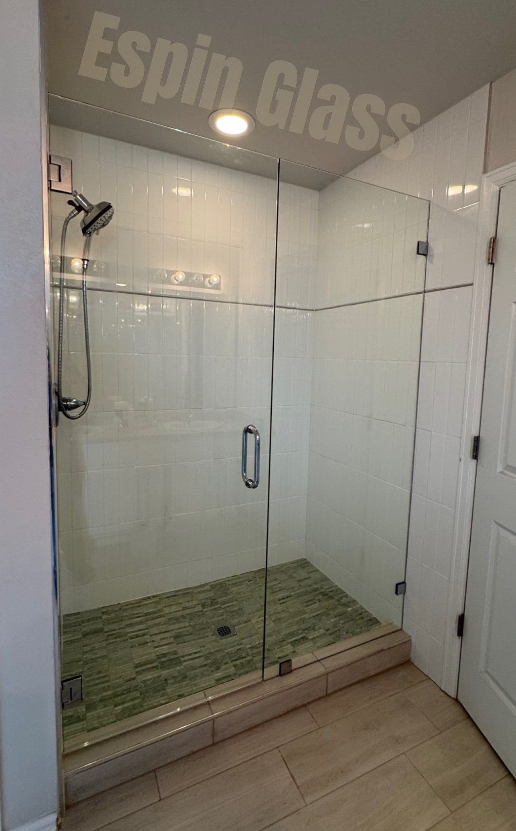 Glass shower enclosure with green tile floor, white subway tile walls, and chrome fixtures.