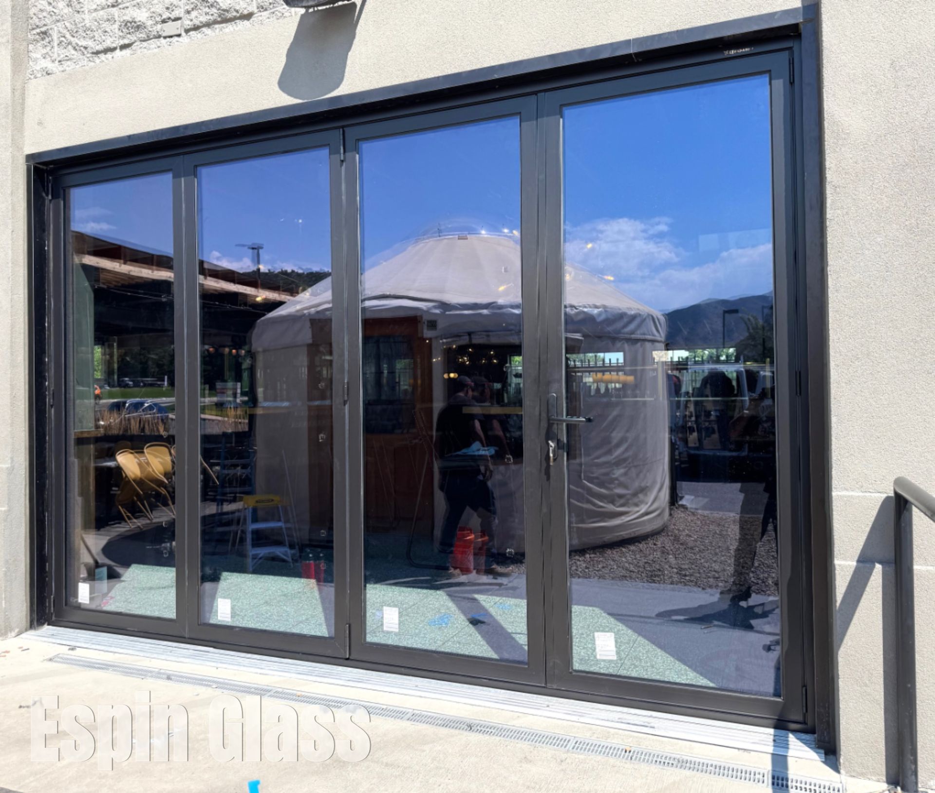 Dark-framed glass doors reflect a yurt and people outside. Exterior shot.