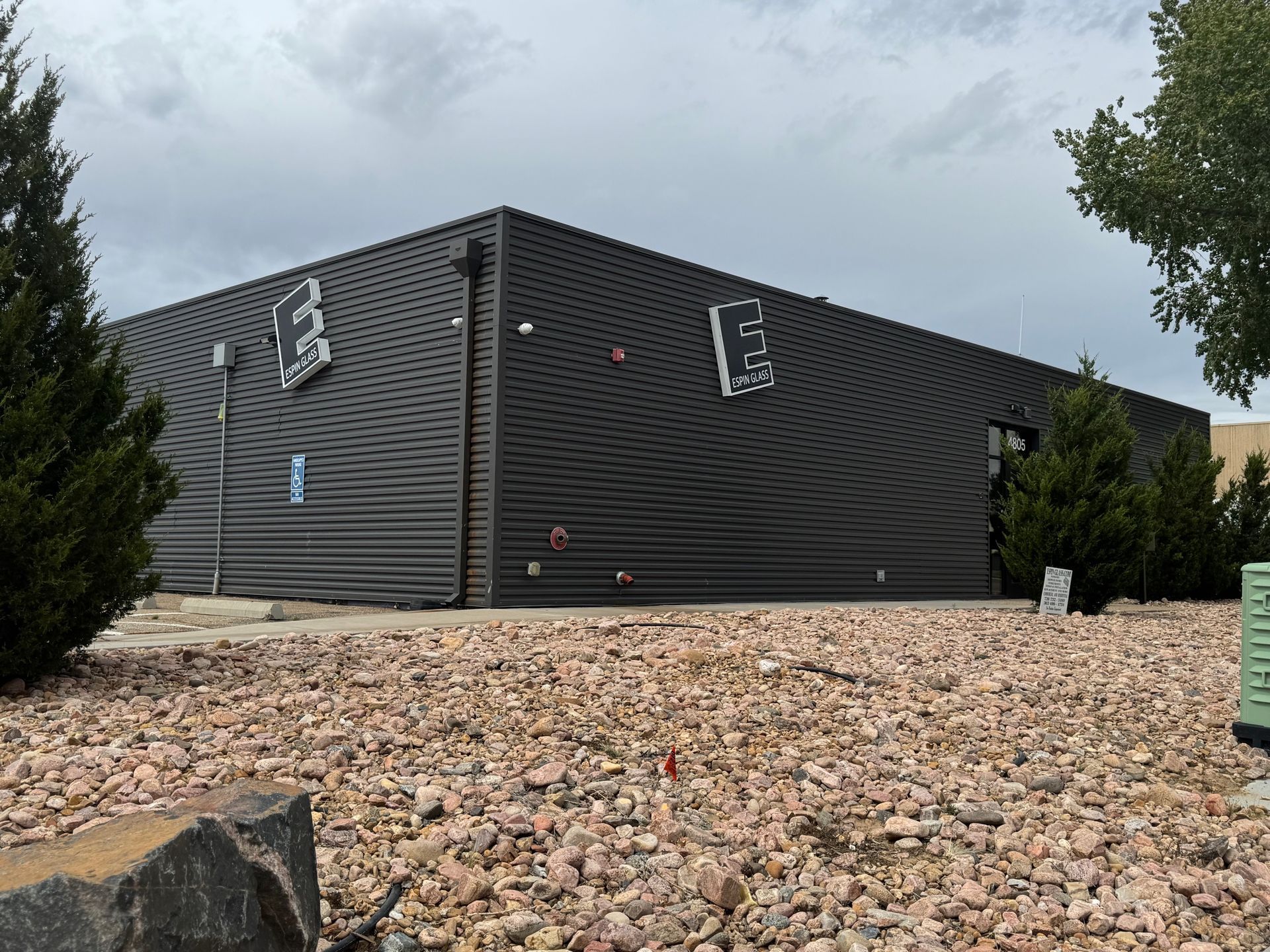 Black building with angled walls, small trees, and reddish-brown gravel ground.